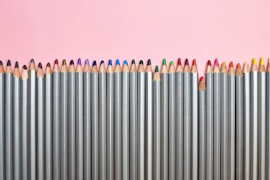 Renkli kalemler pembe arka planda dizilmiş, yaratıcılık ve hobi teması.