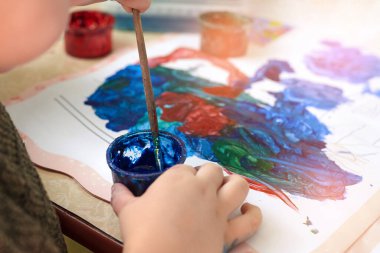 Küçük bir çocuk guaj boyası, eğlence ve çocuk gelişimiyle resim yapıyor..