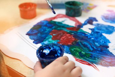 Küçük bir çocuk guaj boyası, eğlence ve çocuk gelişimiyle resim yapıyor..