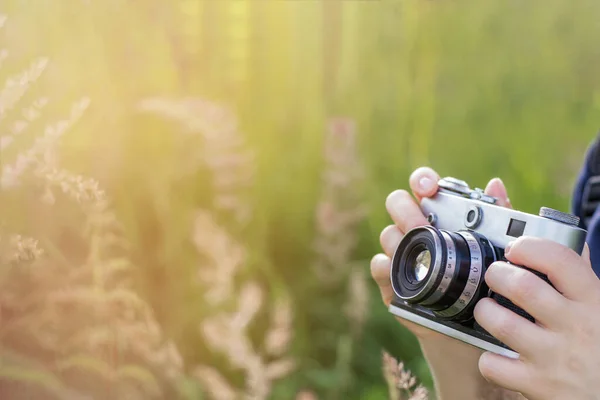 Woman\'s hands are holding a vintage camera outdoors, close-up, copy space, toned photo.