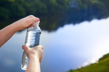 Woman's hands hold plastic bottles with clean drinking water on the background of the river, healthy lifestyle concept.