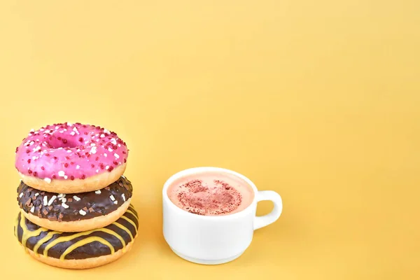 Drei Helle Donuts Neben Einer Tasse Kaffee Auf Gelbem Hintergrund Stockfoto