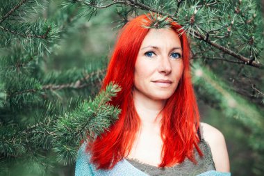 Doğanın arka planında poz veren kızıl saçlı kadın.