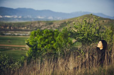 Genç esmer kadın gündüz çimenlerde oturuyor.