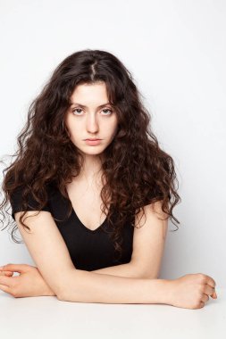 Beyaz arka planda poz veren genç ve duygusal kıvırcık bir kızın portresi.