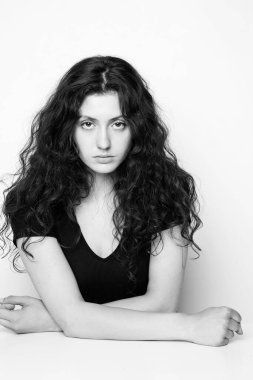 Beyaz arka planda poz veren genç, duygusal, kıvırcık kızın tek renkli portresi.