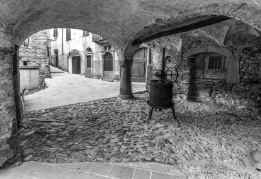 Taş kemerli, geleneksel şarap presi, kaldırım taşı caddesi ve eski binaları olan tarihi Ligurian köyünün siyah ve beyaz görüntüsü