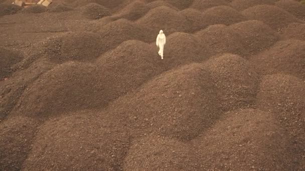 Een man in een wit bacteriologisch pak loopt langs de stenen dijken — Stockvideo