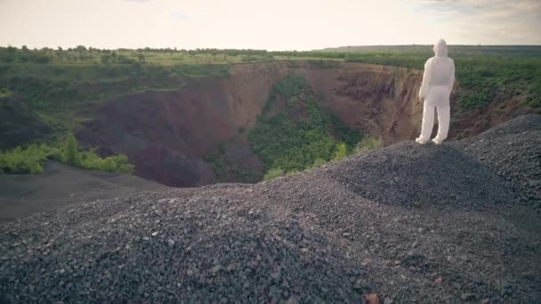 Muž v bílém bakteriologickém ochranném obleku se dívá na obrovskou díru v zemi — Stock video