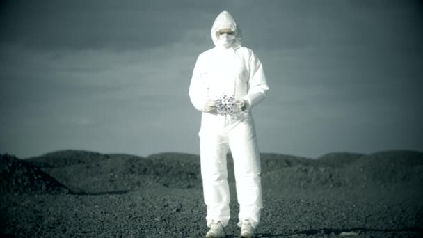 Um cientista num fato de protecção branco num campo de pedra abandonado brinca com uma molécula de vírus — Vídeo de Stock