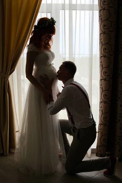 Damat hamile gelinin karnını öper. Tam boy fotoğraf