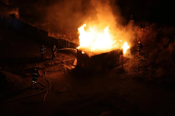 Escouade de quatre pompiers poussant un hangar en flammes — Photo