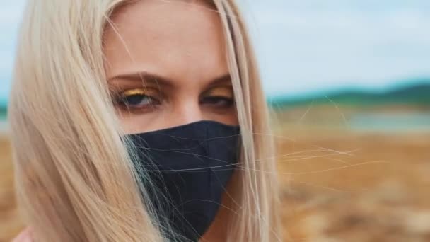 Portret van een lachend, jong meisje met een zwart masker, als gevolg van de coronavirus pandemie en milieuvervuiling. Hij kijkt naar de camera.. — Stockvideo