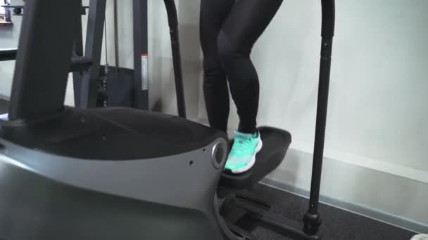 Брюнетка в тренажерному залі тренується на сходинці в чорному костюмі і кросівках. Виконує аеробні кардіо вправи для схуднення. Спалювання жиру — стокове відео