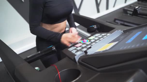 En vacker atletisk brunett flicka tränar i ett gym på ett löpband i en svart sportkläder och sneakers — Stockvideo