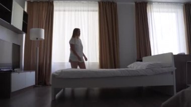 Beyaz tişörtlü ve şortlu yorgun, üzgün bir kadın pencerenin yanındaki yastığa yüzüstü düşer ve uykuya dalar. Stresli hissediyor. Parlak bir yatak odasında zor bir günün ardından rahatla. Evde yalnız