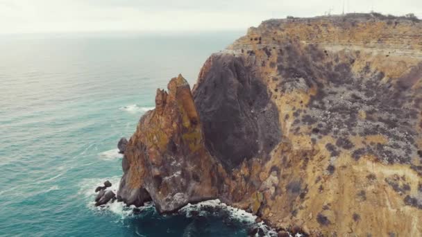 Vista aérea de las olas rompiendo sobre las rocas en el Mar Negro, Cabo Fiolent, la península de Crimea. Volando en un trono sobre fuertes olas marinas que se estrellan sobre afilados acantilados rocosos. Cielo nublado y sombrío — Vídeo de stock