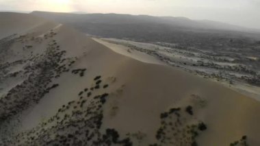 Avrupa 'nın en yüksek kum tepesinin havadan görünüşü, Sarykum Dune, Dağıstan, Rusya. Kumdaki küçük yeşil bitki örtüsü. Dağ sırasının ve ovanın manzarası. Çölün altın kumu. Güneş ışığı 