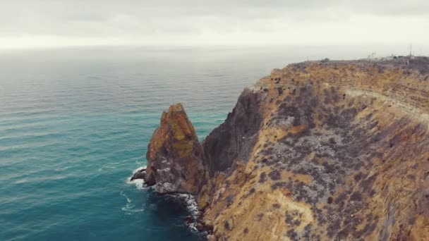 Vista aérea de las olas rompiendo sobre las rocas en el Mar Negro, Cabo Fiolent, la península de Crimea. Volando en un trono sobre fuertes olas marinas que se estrellan sobre afilados acantilados rocosos. Cielo nublado y sombrío — Vídeo de stock