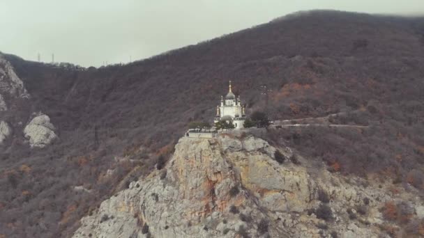 Foros iglesia en la cima de la montaña, Foros, península de Crimea. Vuela sobre la iglesia blanca como la nieve con cúpulas verdes en la cima de la montaña cubiertas de vegetación densa. Iglesia cristiana en el acantilado sobre el Mar Negro — Vídeo de stock