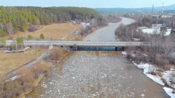 Vue aérienne du cours de la glace sur la rivière. Les gens se tiennent sur le pont au-dessus de la rivière et regardent la glace flotter le long de la rivière. La glace s'est brisée en plusieurs morceaux et la rivière orageuse la porte — Video