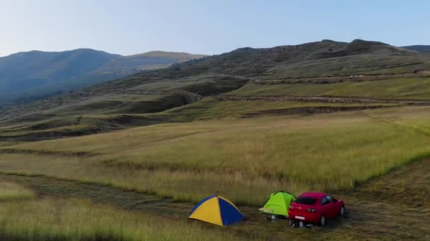 Vue aérienne des touristes qui se réveillent et rencontrent le lever du soleil sur le rocher au Daghestan. Voiture rouge et tentes sur fond de hautes montagnes. Vallée de montagne et verdure sur la crête de pierre du Caucase — Video