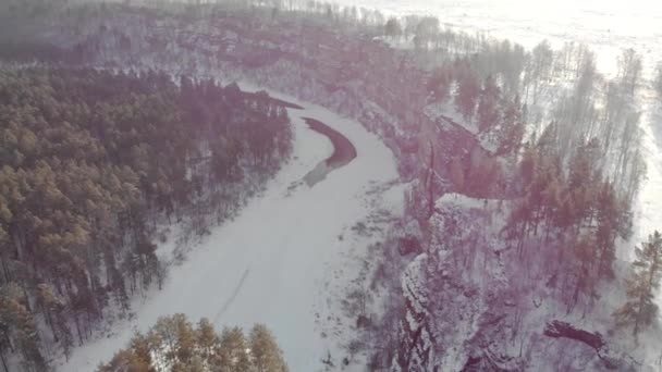 Flygfoto över berg klippa och flod. Frosty kall snöig morgon i södra Ural, Ryssland. Den breda ån är frusen och täckt med is. Människor går på hög sten klippa — Stockvideo
