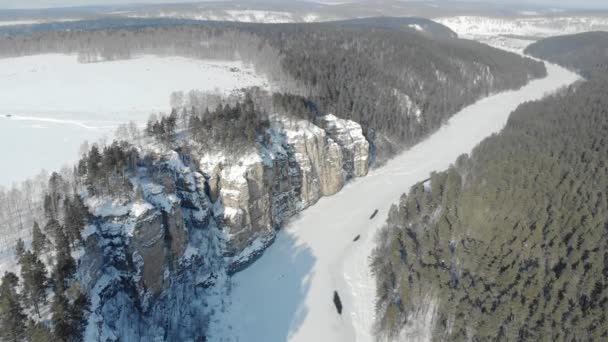 Luftaufnahme der Klippe und des Flusses. Frostig-kalter, schneereicher Morgen im Südural, Russland. Der breite Fluss ist gefroren und mit Eis bedeckt. Menschen gehen auf hohen Steinklippen — Stockvideo