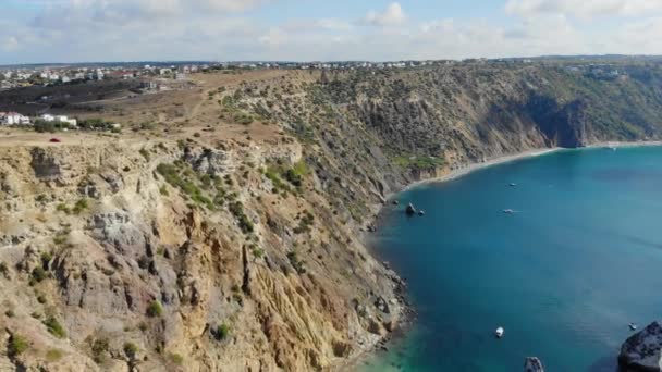 Vista aérea de ondas colidindo contra rochas. Vista superior das ondas azuis do Mar Negro. Carro vermelho no topo da montanha. O navio navega na água. As rochas são visíveis do mar — Vídeo de Stock