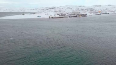 Barents Deniz Koyu 'nun, Atlantik Okyanusu' nun ve Murmansk 'ın hava manzarası. Kış. Körfezin kıyısına yerleşim yeri. Kıyıda farklı renklerde tekneler var. Kuzey Kutup Dairesi 'ndeki insanların hayatı.