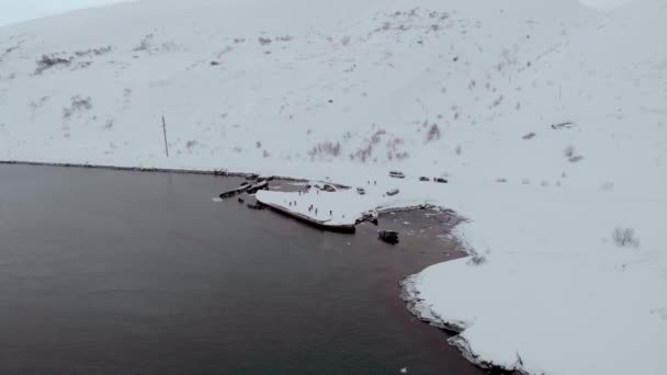 Légi felvétel a hajó temetőjéről, Teriberka, Murmanszk. A turisták a Barents-tenger homokos partján sétálnak, amelyet hó borít. Tél. Félelmetes hajócsontvázak állnak ki a vízből. — Stock videók