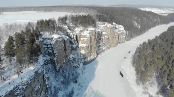 Luchtfoto van bergklif en rivier. IJzige koude sneeuwochtend in de Zuid-Oeral, Rusland. De brede rivier is bevroren en bedekt met ijs. Mensen lopen op hoge stenen klif — Stockvideo