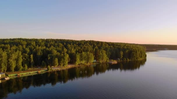 Vue aérienne du coucher du soleil sur un lac bleu clair profond. Des arbres luxuriants épais poussent sur les rives. Légère brise soufflant. Des ondulations traversent le lac. Le soleil joue avec la lumière. L'été. L'apaisement. Tourisme en Russie — Video