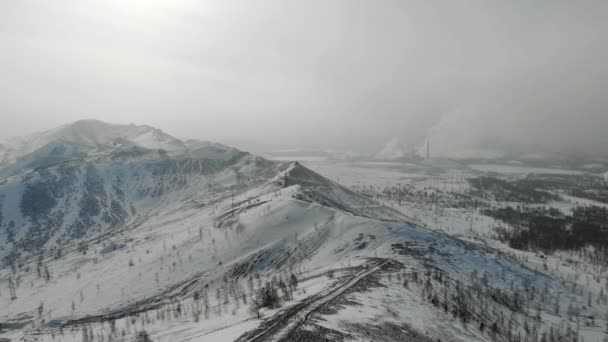 Vista aérea de fábrica. Las colinas de invierno están cubiertas de nieve. Detrás de cables y soportes eléctricos. Acrid humo venenoso proviene de las chimeneas de la planta. Contaminación ambiental — Vídeo de stock