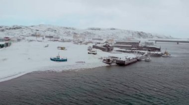 Barents Deniz Koyu 'nun, Atlantik Okyanusu' nun ve Murmansk 'ın hava manzarası. Kış. Körfezin kıyısına yerleşim yeri. Kıyıda farklı renklerde tekneler var. Kuzey Kutup Dairesi 'ndeki insanların hayatı.