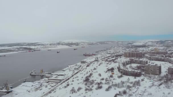 Vista aérea del puerto marítimo, Murmansk, Rusia. Largas salas de producción en las costas nevadas del mar de Barents. Descarga y carga de materiales en los buques. Grandes grúas de hierro en las orillas. Vida polar — Vídeos de Stock