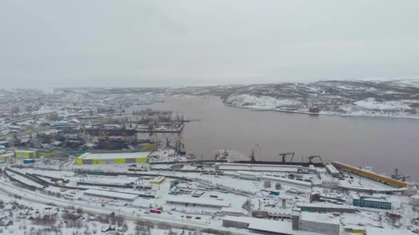 Luchtfoto van de zeehaven, Moermansk, Rusland. Lange productiehallen aan de besneeuwde kusten van de Barentszzee. Lozen en laden van materialen op schepen. Grote ijzeren kranen op de oevers. IJsleven — Stockvideo