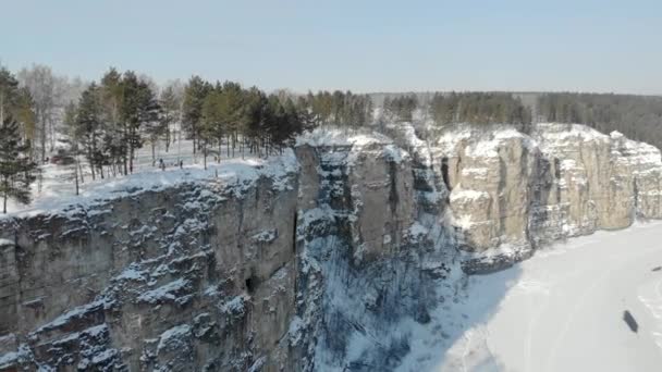 Luchtfoto van bergklif en rivier. IJzige koude sneeuwochtend in de Zuid-Oeral, Rusland. De brede rivier is bevroren en bedekt met ijs. Mensen lopen op hoge stenen klif — Stockvideo