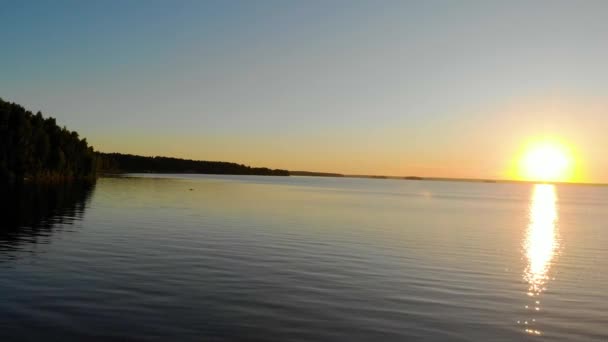 Vista aérea de la puesta del sol en el lago azul profundo claro. Gruesos árboles exuberantes crecen en las orillas. Soplando brisa ligera. Las olas cruzan el lago. El sol juega con la luz. Verano. Appeasement. Turismo en Rusia — Vídeos de Stock