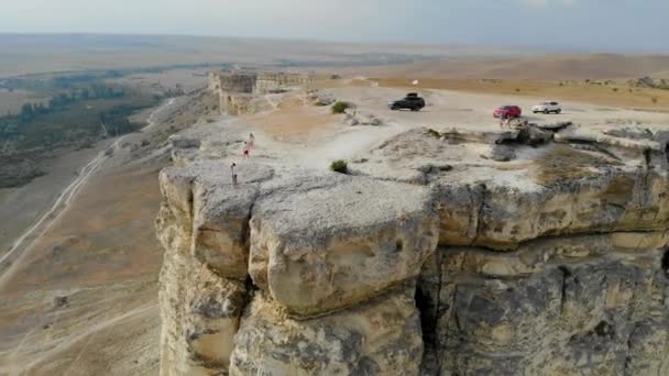 Vista aérea de White Rock, península de Crimea. Hay coches en la cima del alto acantilado. Los turistas pasean por la meseta rocosa. Los senderos corren desde el fondo de la montaña, los campos se vuelven verdes — Vídeos de Stock