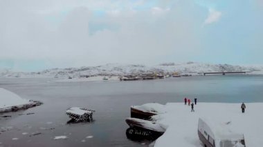 Gemi mezarlığının havadan görünüşü, Teriberka, Murmansk. Turistler, Barents Denizi 'nin karla kaplı kumlu sahillerinde yürüyorlar. Kış. Korkutucu gemi iskeletleri sudan dışarı sarkıyor.