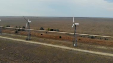 Rüzgar türbinlerinin hava görüntüsü. Boş tarlanın arka planında çiftlik rüzgârı türbinleri. Sakin hava ve rüzgar türbinleri hareket olmadan çalışmaz. Rüzgar türbinleri boyunca giden yollar mesafeye çıkıyor.