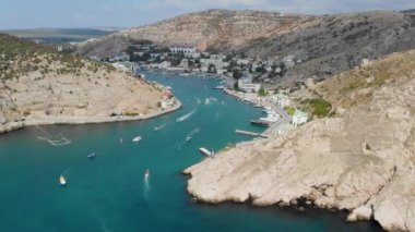 Sivastopol 'daki Balaklava Körfezi' nin havadan görüntüsü. Tekneler Karadeniz boyunca ilerleyip arkalarında dalgalar bırakır. Eski Chembalo kalesi dağda yer almaktadır.