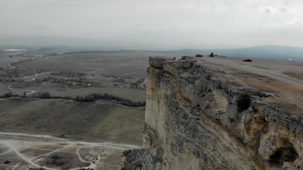 Luchtfoto van White Rock, Krim schiereiland. Er staan auto 's bovenaan de hoge klif. Toeristen wandelen over het rotsplateau. Trails lopen vanaf de bodem van de berg, velden worden groen — Stockvideo