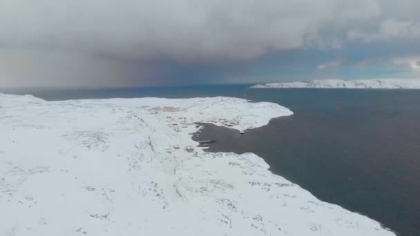 Αεροφωτογραφία του Κόλπου Μπάρεντς, Ατλαντικός Ωκεανός, Μουρμάνσκ. Η γαλάζια θάλασσα ξεσπά σε λευκά κύματα στις ακτές στις οποίες βρίσκονται τα σπίτια. Καταιγίδα. Το έδαφος είναι καλυμμένο με χιόνι. Χειμώνας. Τουρισμός — Αρχείο Βίντεο