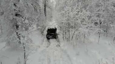 Siyah SUV 'un dağların arasındaki patika boyunca derin beyaz karlar boyunca ilerleyişini gösteren hava manzarası. Cip karlı dağların, uzun çamların ve köknar ağaçlarının arasına sıkıştı. Sıra dışı seyahat, turizm