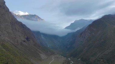 Ritsa Gölü, Abhazya, Dağ Geçidi 'nin havadan görünüşü. Yamaçlar yeşilliklerle kaplı. Bulutların arasında saklanan keskin dağlar var. Aşağıdaki dağ nehri boyunca uzanan yollar var.