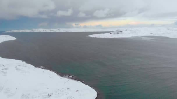 Vue aérienne de la baie de Barents, océan Atlantique, Mourmansk. La mer bleue se brise en vagues blanches sur les rives sur lesquelles les maisons sont situées. Tempête. Le sol est couvert de neige. L'hiver. Tourisme — Video