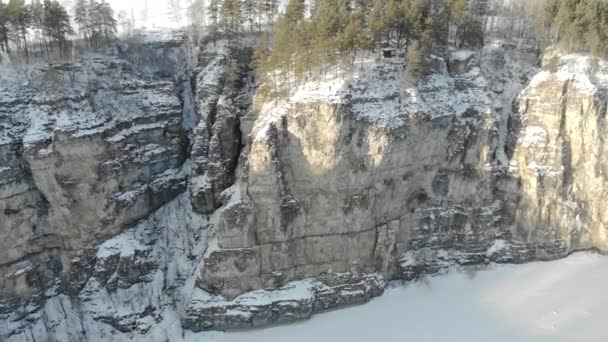 Luftaufnahme der Klippe und des Flusses. Frostig-kalter, schneereicher Morgen im Südural, Russland. Der breite Fluss ist gefroren und mit Eis bedeckt. Menschen gehen auf hohen Steinklippen — Stockvideo