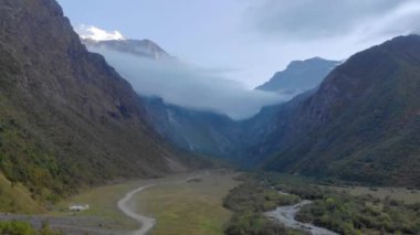 Ritsa Gölü, Abhazya, Dağ Geçidi 'nin havadan görünüşü. Yamaçlar yeşilliklerle kaplı. Bulutların arasında saklanan keskin dağlar var. Aşağıdaki dağ nehri boyunca uzanan yollar var.